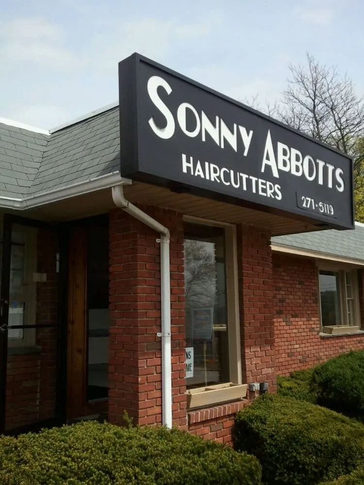 Black sign reading Sonny Abbotts Haircutters above a red brick storefront with a slate roof.