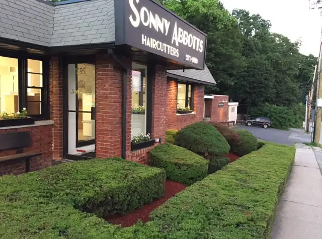 The red brick storefront at dusk, with its black sign, lit windows and clipped hedges.