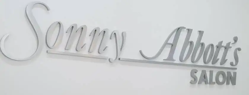 Sonny Abbott’s Salon in brushed metal script on a white wall.