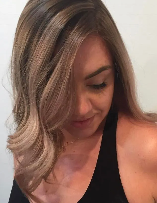 Ash blonde balayage with a soft curl at the ends, on a client looking down.