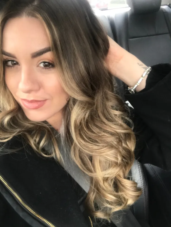 Client with curled brown hair and blonde balayage through the ends.